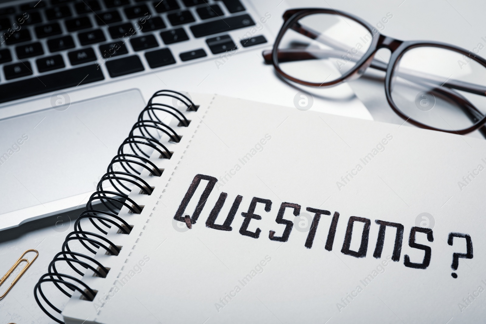 Photo of Word QUESTIONS written in notebook, eyeglasses and laptop on table, closeup