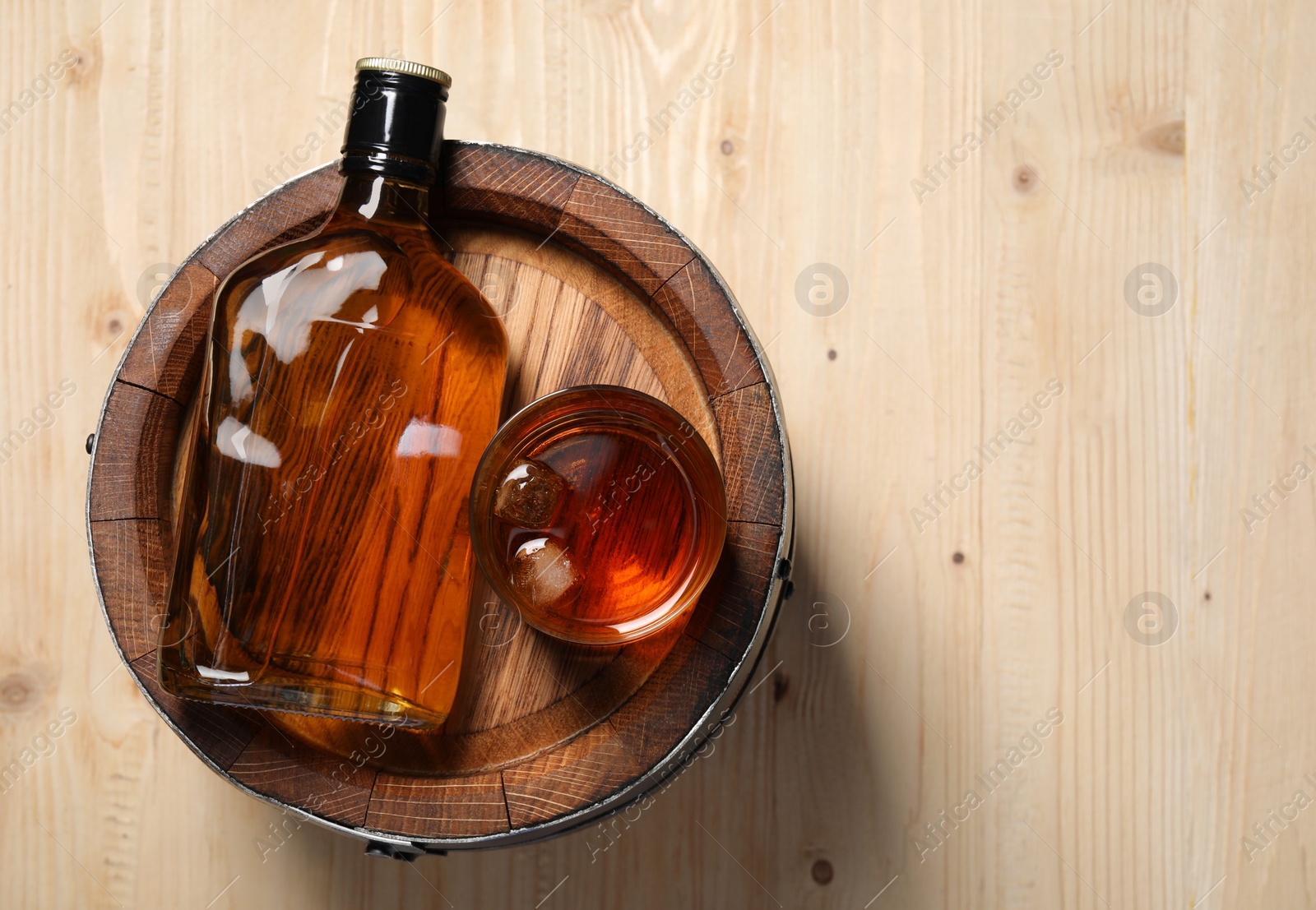 Photo of Barrel, bottle and glass of tasty whiskey on wooden table, top view. Space for text