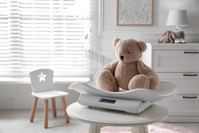 Baby scales with teddy bear on table in room