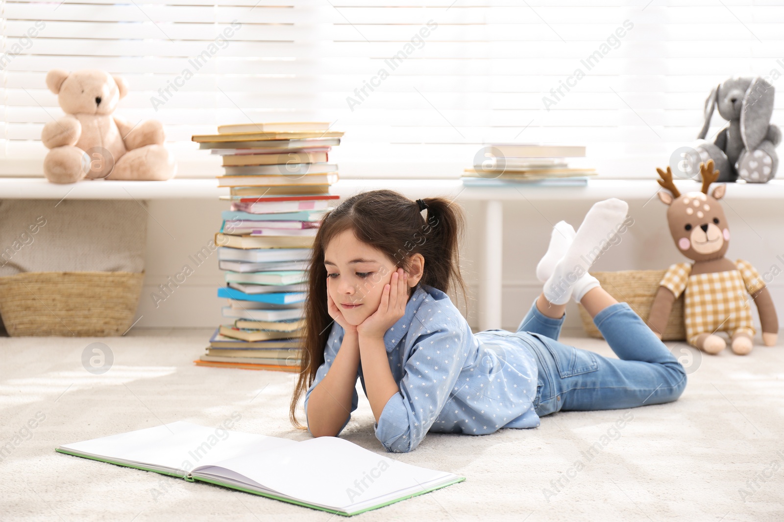 Photo of Little girl reading book on floor at home