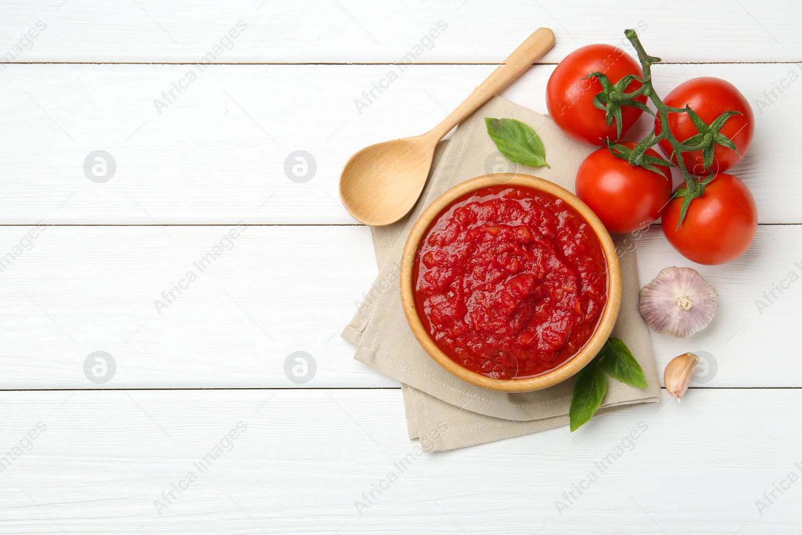 Photo of Homemade tomato sauce in bowl, spoon and fresh ingredients on white wooden table, flat lay. Space for text