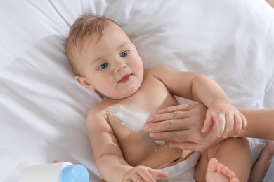 Photo of Mother applying dusting powder onto her baby on bed, top view