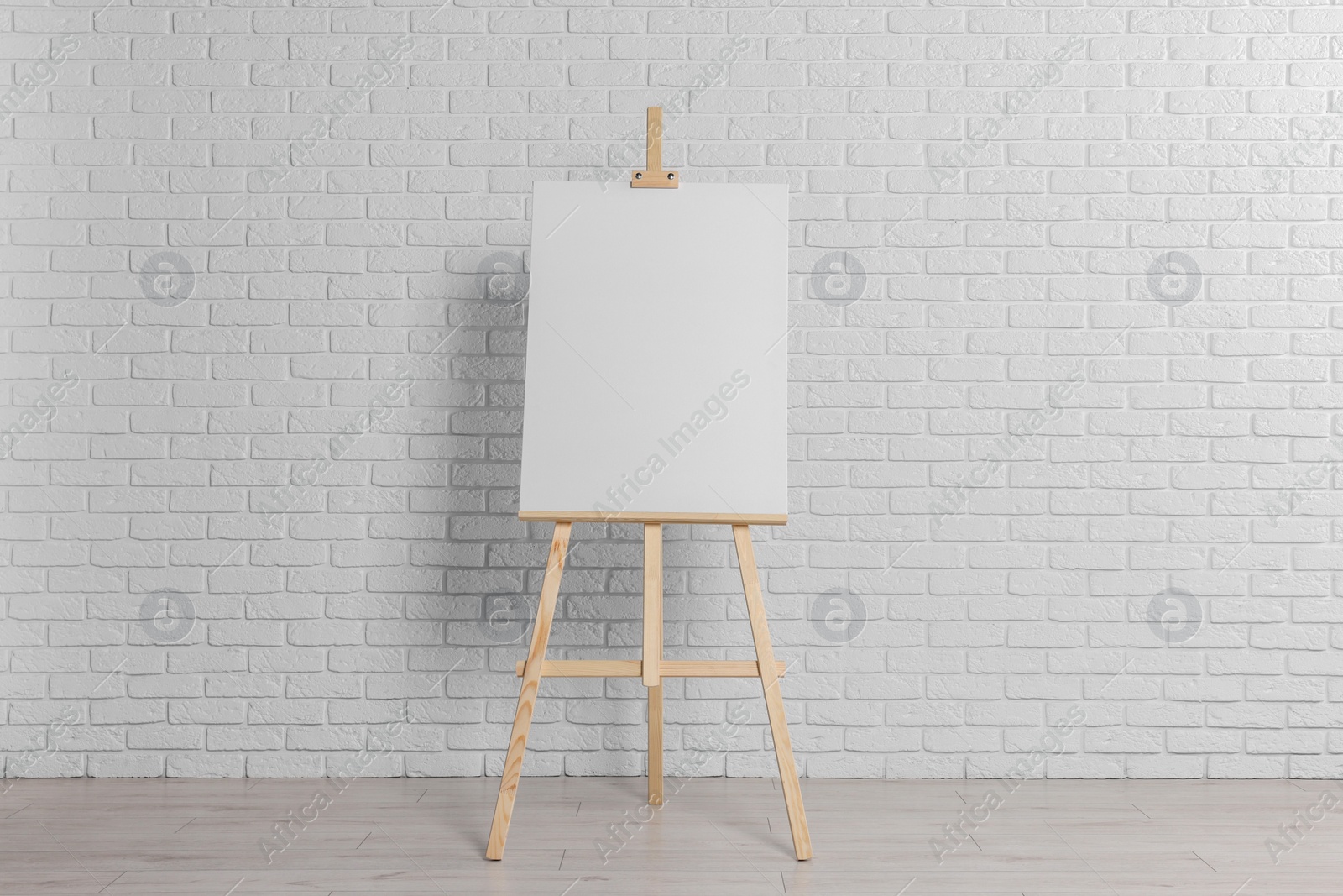 Photo of Wooden easel with blank canvas near white brick wall indoors