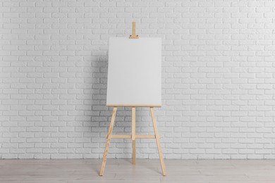 Wooden easel with blank canvas near white brick wall indoors