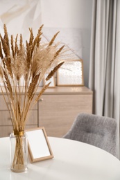 Dry plants and photoframe on white table indoors. Interior design