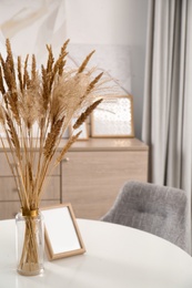 Photo of Dry plants and photoframe on white table indoors. Interior design