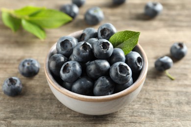 Photo of Bowl of tasty fresh blueberries on wooden table, closeup