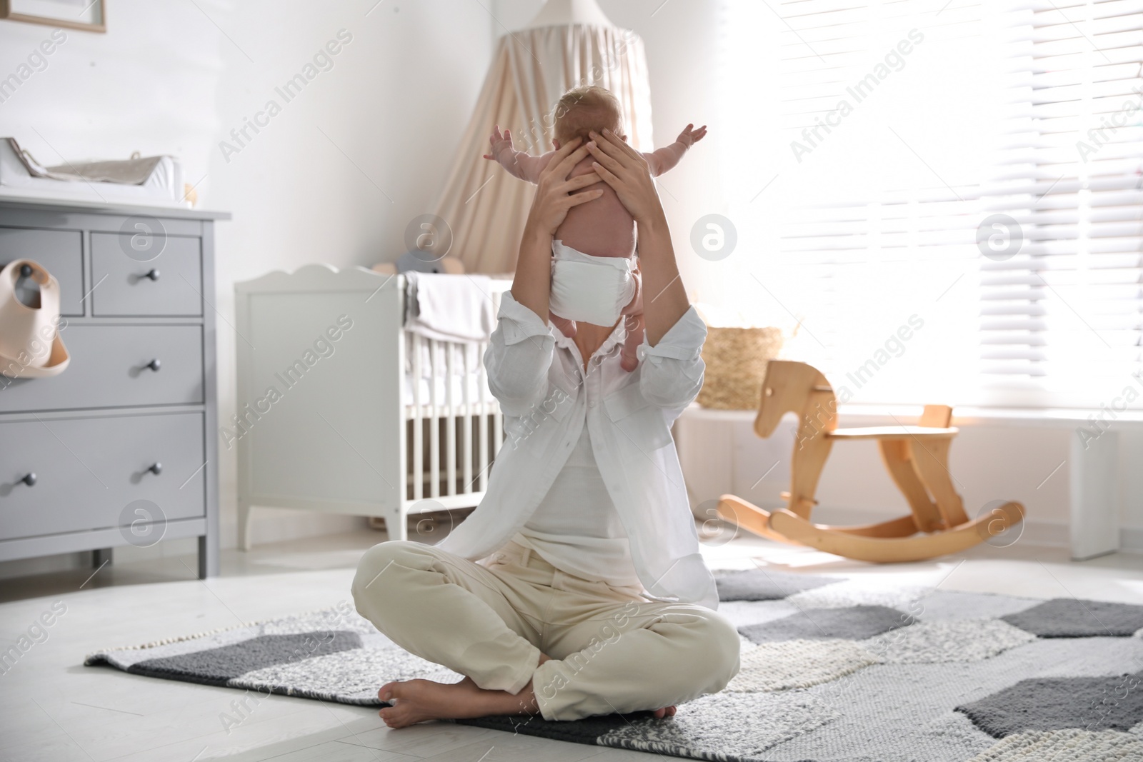 Photo of Young mother with her little baby sitting on floor at home