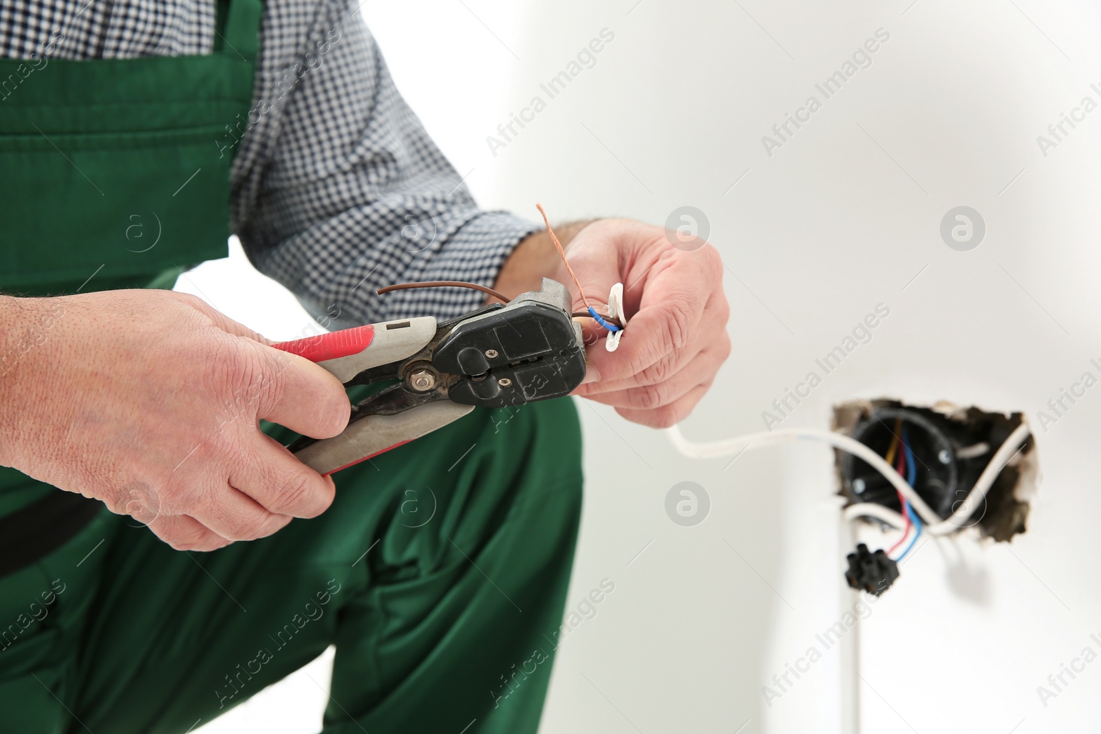 Photo of Professional electrician stripping wire ends indoors, closeup