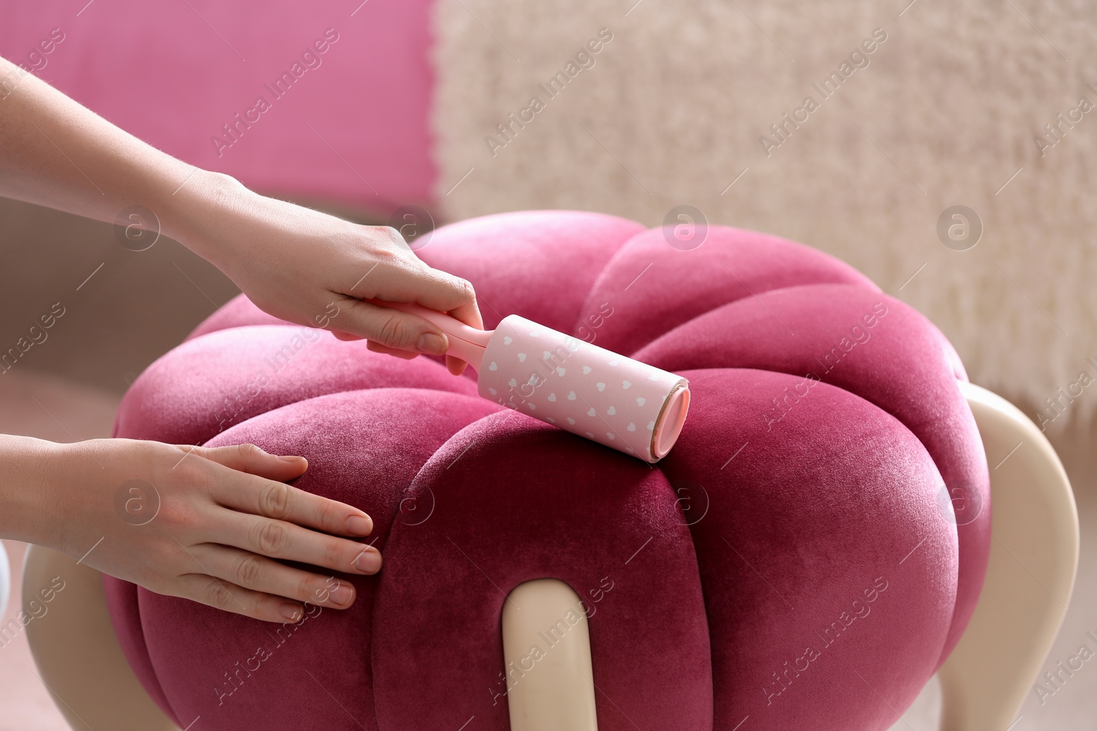 Photo of Woman cleaning pink pouf with lint roller at home, closeup