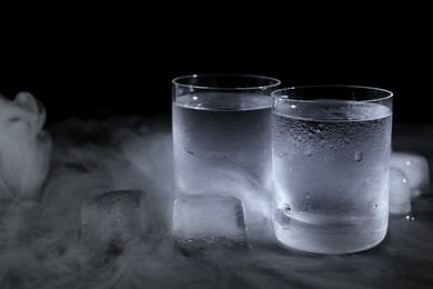 Photo of Vodka in shot glasses with ice on table against black background, closeup