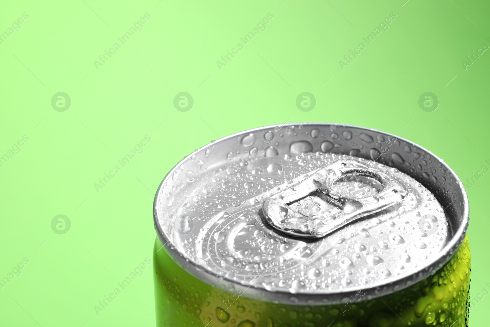 Photo of Aluminum can of beverage covered with water drops on green background, closeup. Space for text