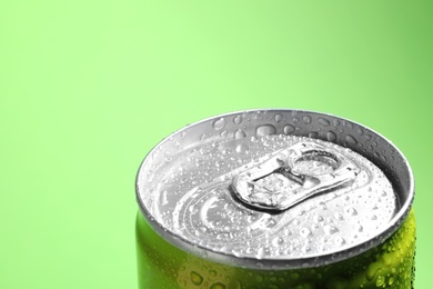 Photo of Aluminum can of beverage covered with water drops on green background, closeup. Space for text