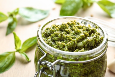 Photo of Jar of tasty pesto sauce on table, closeup. Space for text
