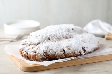 Photo of Delicious Stollen sprinkled with powdered sugar on wooden table