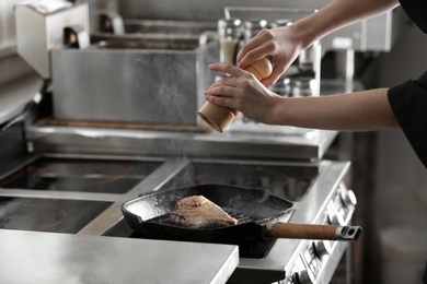 Female chef cooking meat on stove in restaurant kitchen, closeup