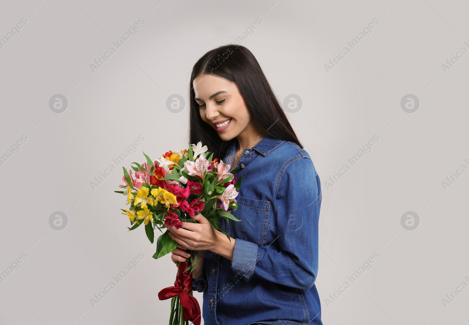 Photo of Happy young woman with beautiful bouquet on light grey background