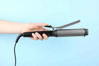 Photo of Hair styling appliance. Woman holding curling iron on light blue background, closeup