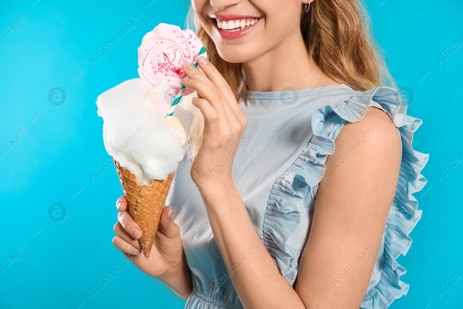 Photo of Young woman holding cotton candy dessert on blue background, closeup