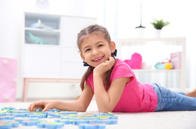 Cute child playing with puzzle on floor at home