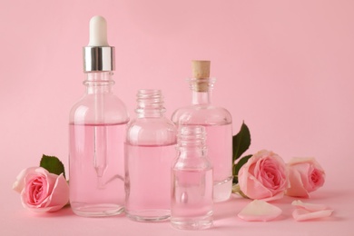 Bottles of essential oil and roses on pink background