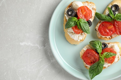 Photo of Plate of delicious tomato bruschettas on light grey marble background, top view. Space for text