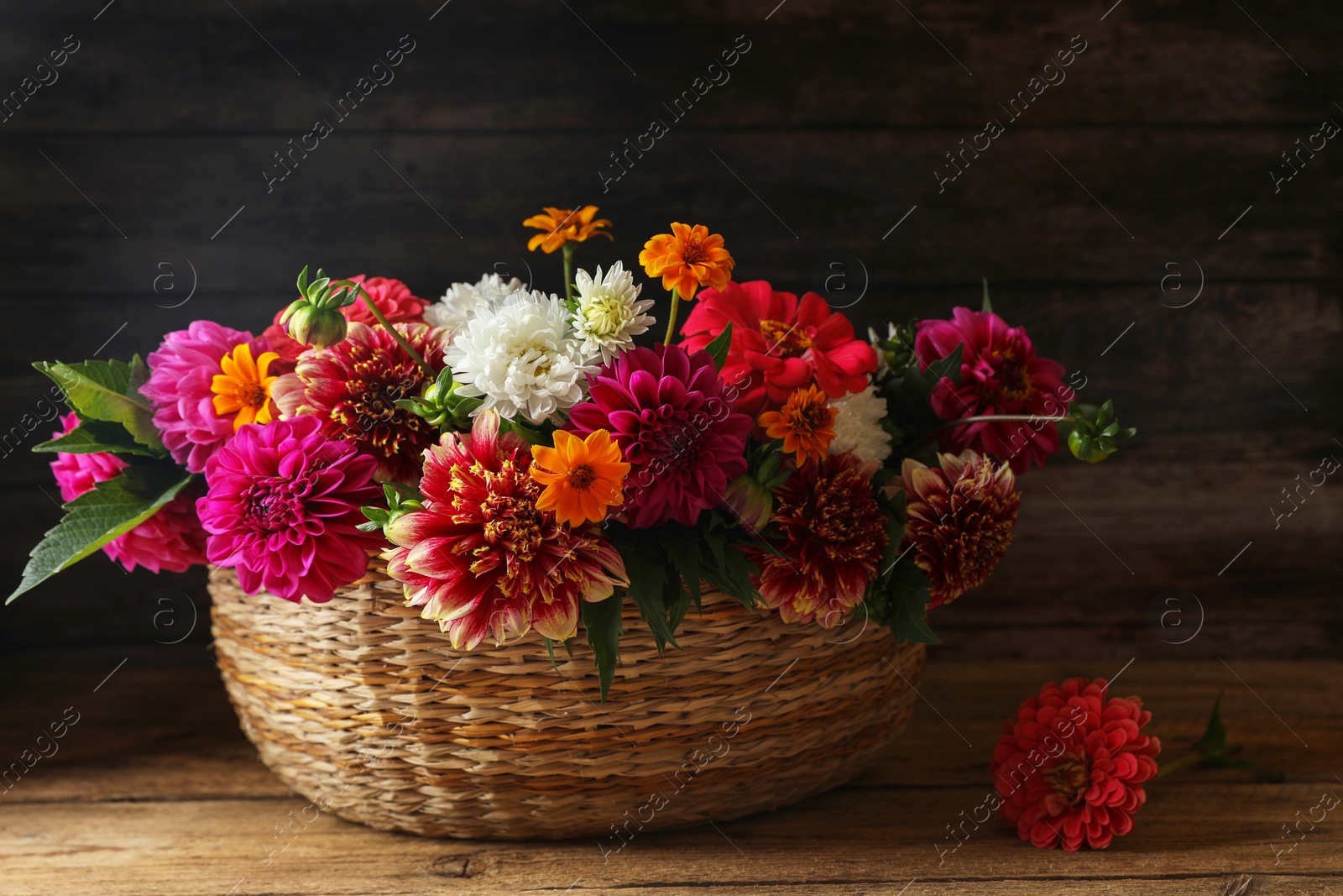 Photo of Beautiful wild flowers and leaves in wicker basket on wooden table