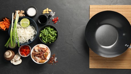 Flat lay composition with black wok, spices and products on dark textured table
