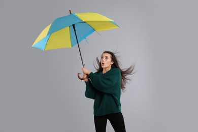 Emotional woman with umbrella caught in gust of wind on grey background
