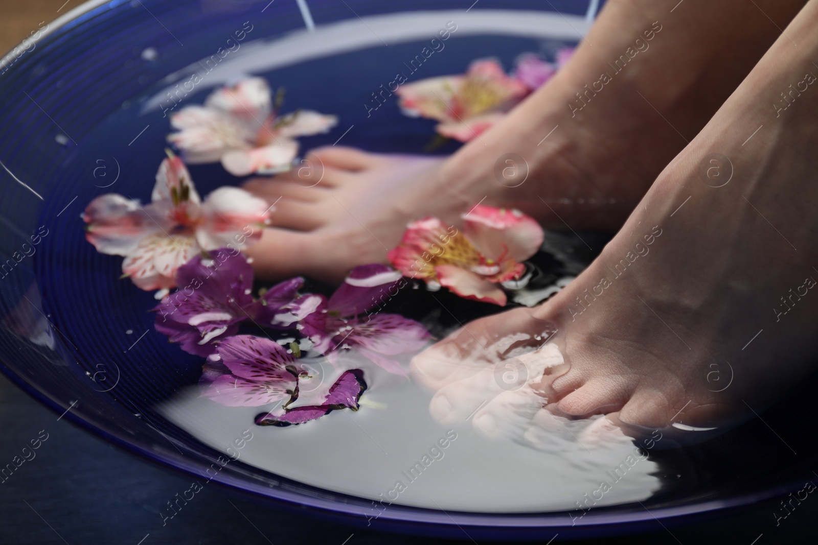 Photo of Woman soaking her feet in bowl with water and flowers, closeup. Spa treatment