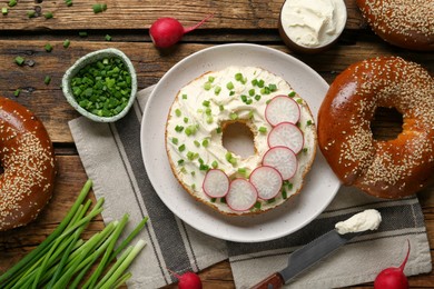 Photo of Delicious bagel with cream cheese, green onion and radish on wooden table, flat lay