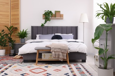 Stylish bedroom with double bed and beautiful green houseplants. Modern interior