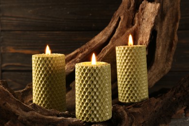 Beautiful burning beeswax candles on snag near wooden wall