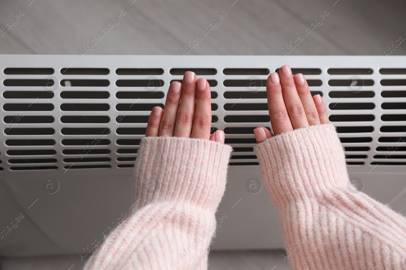 Photo of Woman warming hands near electric heater at home,  top view