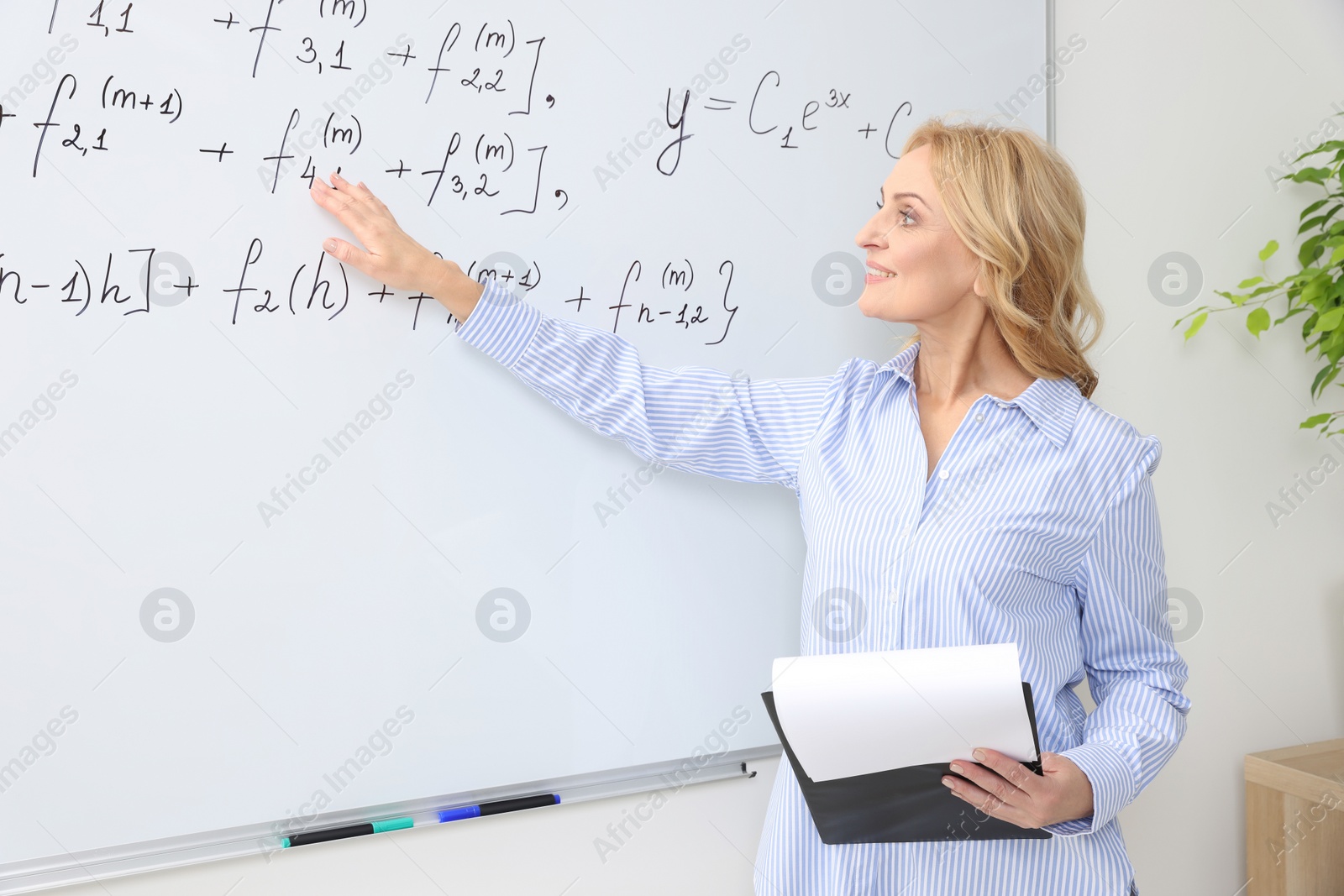 Photo of Professor with clipboard giving lecture near whiteboard in classroom