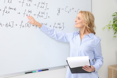 Photo of Professor with clipboard giving lecture near whiteboard in classroom