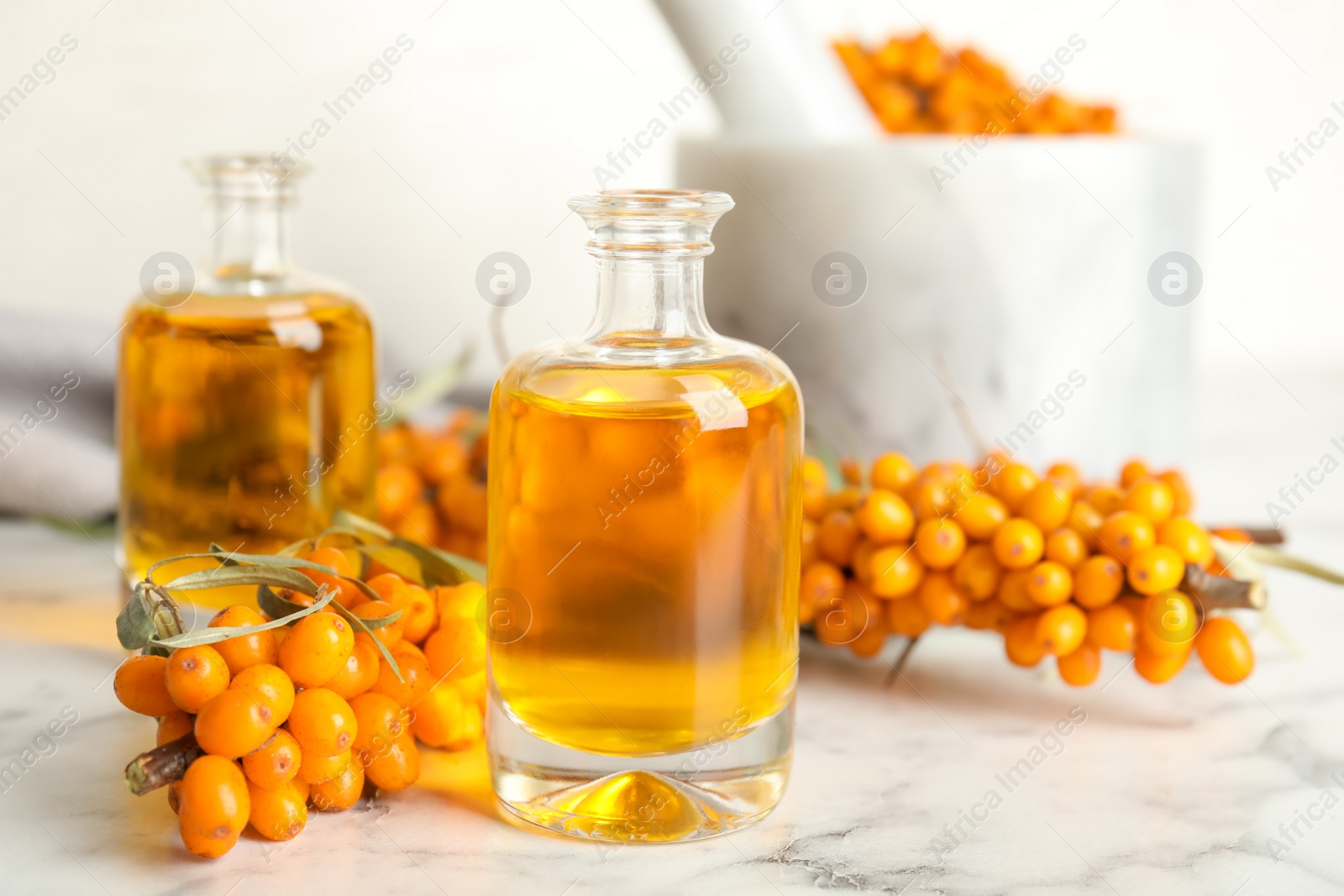 Photo of Natural sea buckthorn oil and fresh berries on white marble table