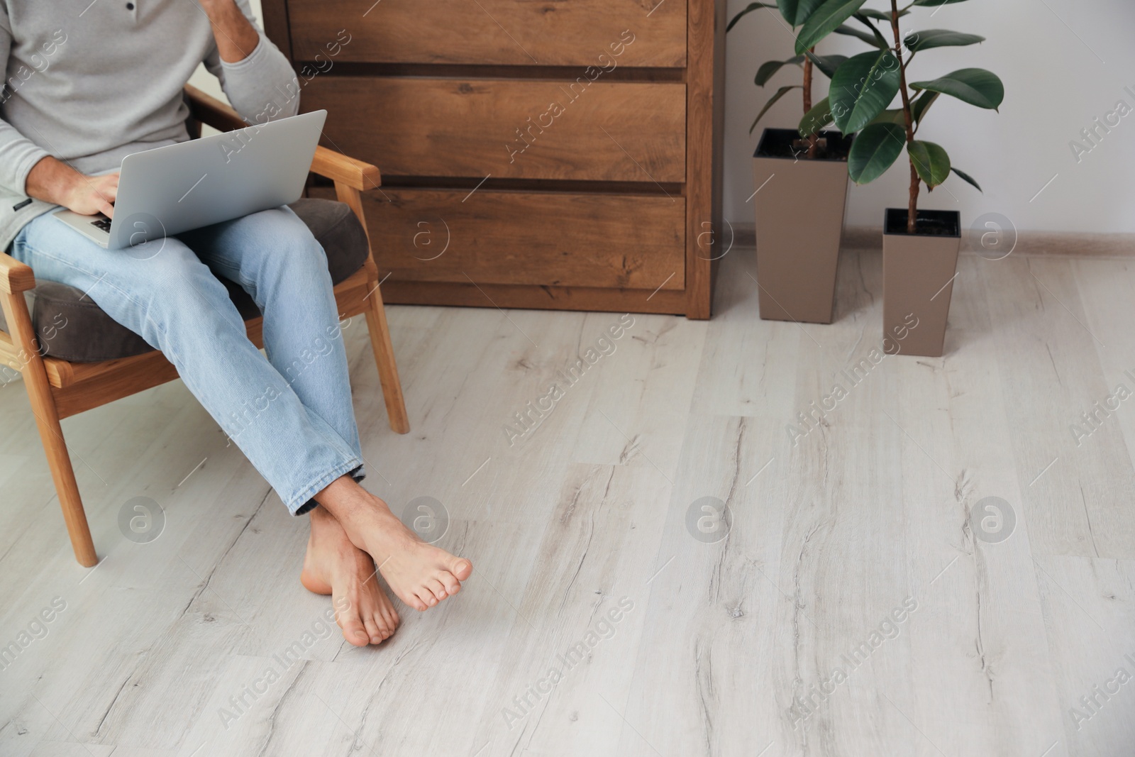 Photo of Man with laptop sitting in armchair at home, closeup. Floor heating system