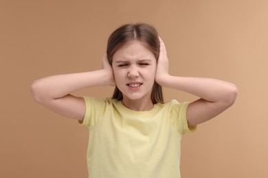 Photo of Hearing problem. Little girl suffering from ear pain on pale brown background
