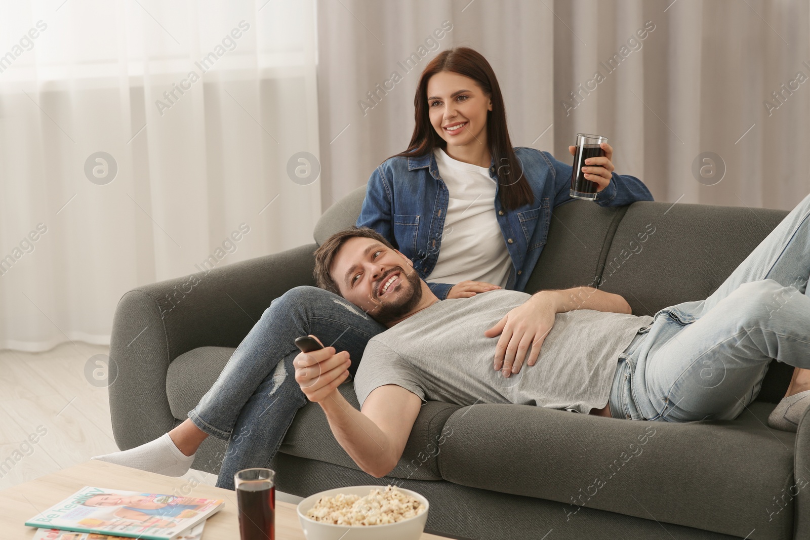 Photo of Happy couple watching show at home. Man changing TV channels with remote control