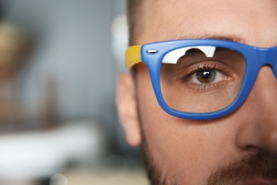 Young man wearing glasses on blurred background, closeup. Ophthalmology service