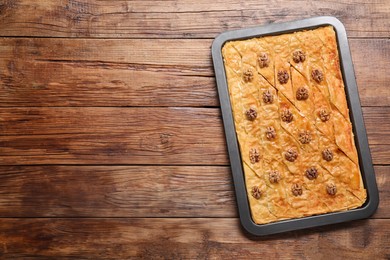Delicious baklava with walnuts in baking pan on wooden table, top view. Space for text