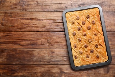 Photo of Delicious baklava with walnuts in baking pan on wooden table, top view. Space for text