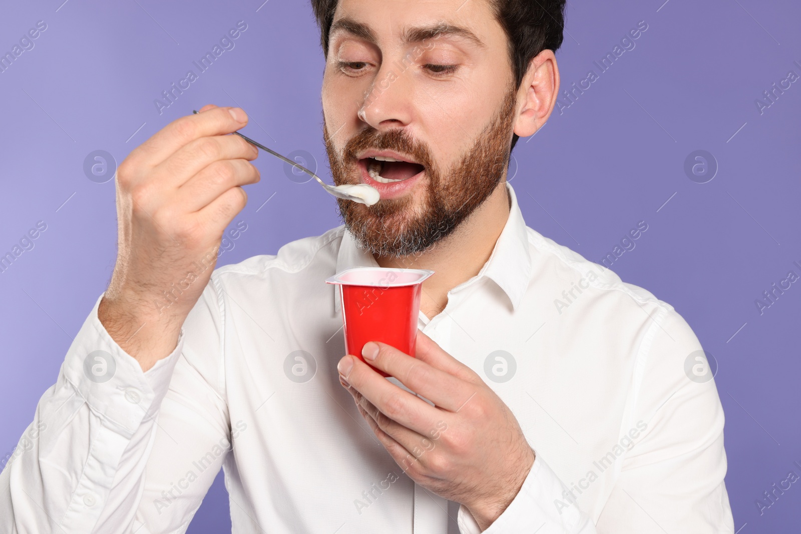 Photo of Handsome man eating delicious yogurt on violet background