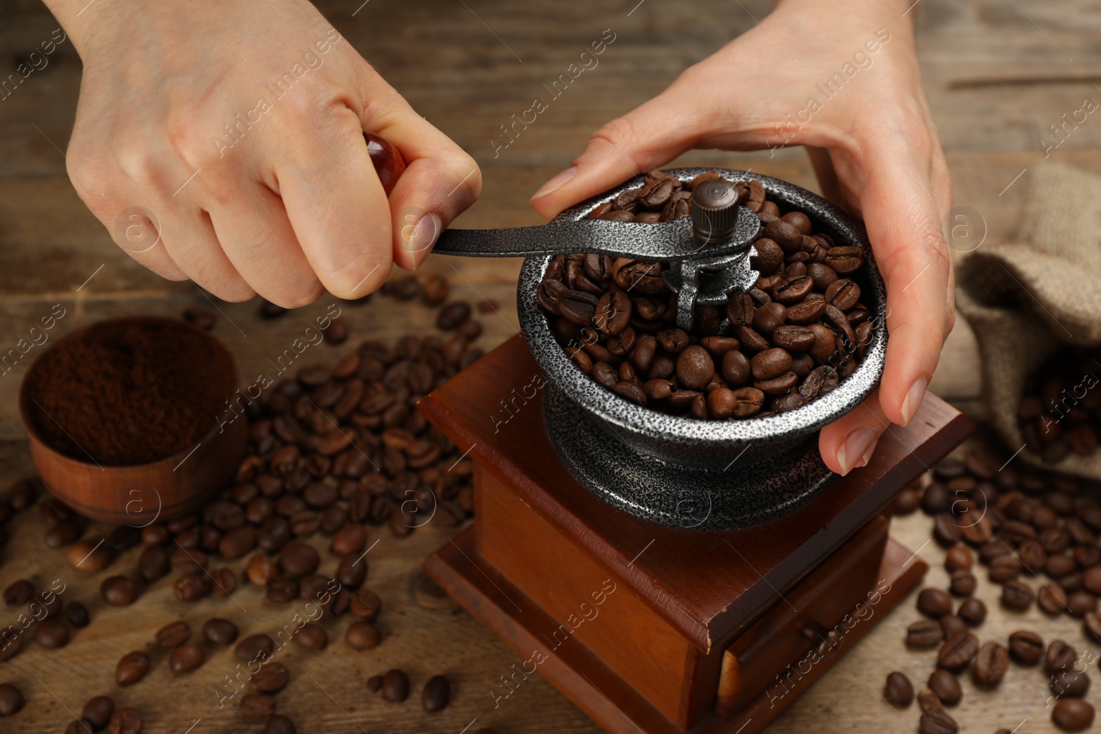 Photo of Woman using manual coffee grinder at wooden table, closeup