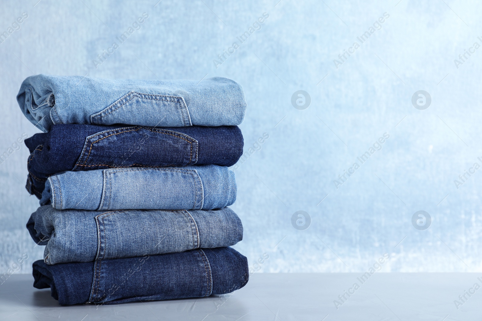 Photo of Stack of different jeans on light table against blue background. Space for text