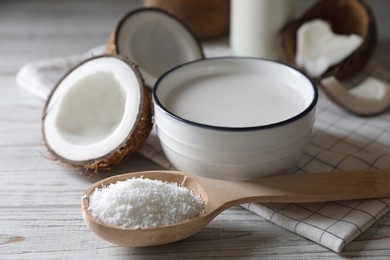 Bowl of delicious coconut milk, spoon with flakes and nuts on white wooden table, closeup