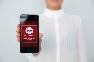 Photo of Woman holding smartphone with warning about virus attack on white background, closeup