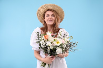 Beautiful woman in straw hat with bouquet of flowers on light blue background