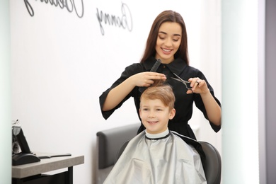 Photo of Professional female hairdresser working with little boy in salon